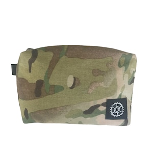 K&ouml;nnte beinhalten: Eine Tasche in Tarnmuster mit einem schwarzen Rei&szlig;verschluss und einem kleinen schwarzen Patch mit einem wei&szlig;en Logo in der unteren rechten Ecke.