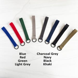 May include: Eight keychains in different colors, including blue, red, green, light grey, charcoal grey, navy, black, and khaki. Each keychain has a metal ring.