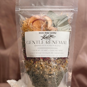 May include: A clear plastic bag filled with a simmer pot potion blend. The label reads "GENTLE RENEWAL" with the text "CALM MY HEART + EASE MY MIND, LEAVE WHAT WEIGHS ME FAR BEHIND." The blend includes dried flowers, herbs, and apple slices. The bag is resting on a white, crystalline surface.