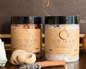 May include: Two clear plastic jars with black lids containing ritual bath salts. The left jar is labeled Full Moon Ritual Bath Salts, cleanse-release-uplift. The right jar is labeled New Moon Ritual Bath Salts, manifest-new beginnings-focus, High Vibe Home.