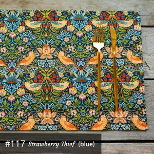 May include: A blue and green table runner with a floral pattern and birds. The runner has a gold fork and knife on top of it. #117 Strawberry Thief (blue)
