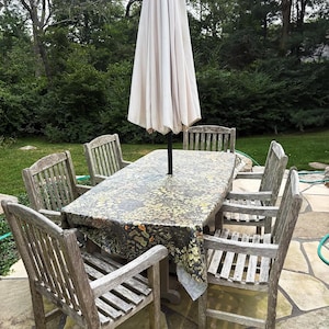 Peut inclure: Ensemble de salle à manger d'extérieur avec une table rectangulaire, six chaises en bois et un parasol beige. La table est recouverte d'une nappe à motifs. Les chaises et la table ont un aspect vieilli.