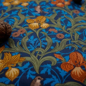 Könnte beinhalten: Nahaufnahme eines blauen Stoffes mit einem Blumenmuster. Der Stoff zeigt orange, gelbe und grüne Blumen sowie kleine braune Vögel. Eine braune Walnuss befindet sich im Vordergrund.