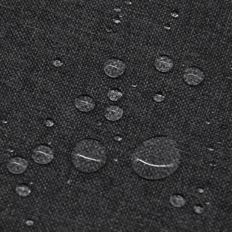 May include: A dark gray fabric with a visible woven texture featuring multiple clear water droplets scattered across the surface. The droplets vary in size and create a beaded effect on the material, highlighting its water-repellent quality.