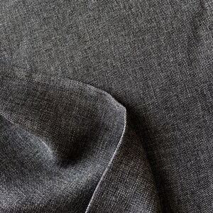 May include: A dark charcoal gray fabric with a visible woven texture and a tight, uniform weave pattern. The material is folded over itself, creating a soft curve and a subtle shadow along the edge, highlighting the dense, matte textile surface.