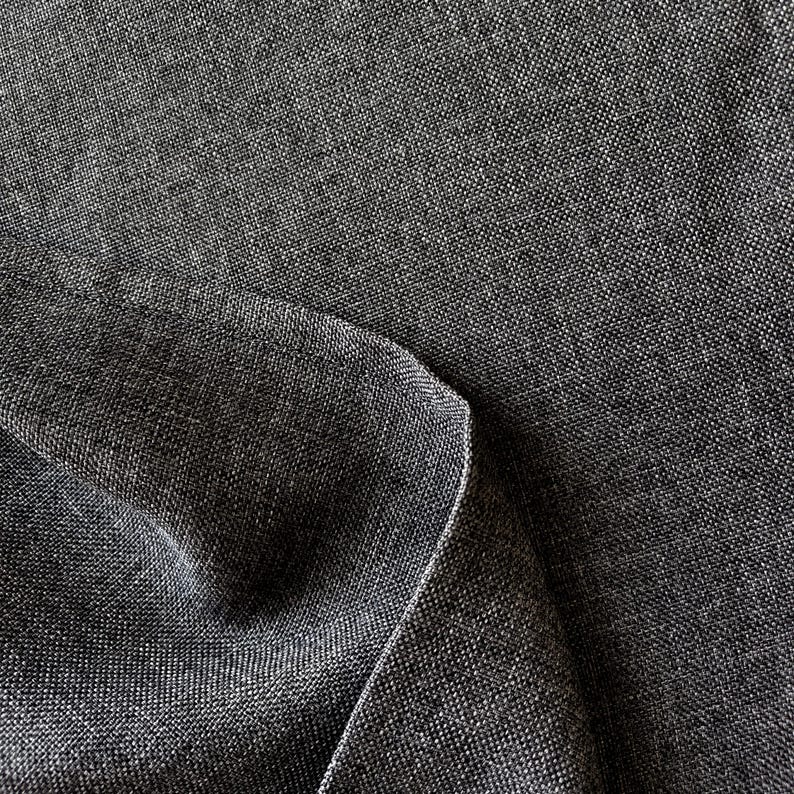May include: A dark charcoal gray fabric with a visible woven texture and a tight, uniform weave pattern. The material is folded over itself, creating a soft curve and a subtle shadow along the edge, highlighting the dense, matte textile surface.
