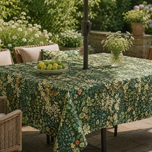 May include: A square tablecloth featuring a dense botanical print of green leaves, small white flowers, and orange accents. The fabric covers a patio table with a central umbrella pole, holding a white bowl filled with yellow and green limes.