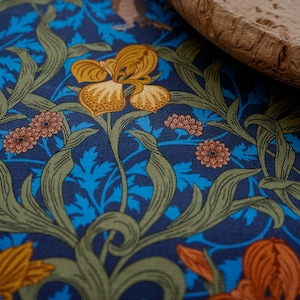 Könnte beinhalten: Eine Nahaufnahme eines blauen Stoffes mit einem Blumenmuster. Der Stoff zeigt gelbe, orange und grüne Blumen mit braunen Akzenten. Der Stoff ist strukturiert und hat einen Vintage-Look.