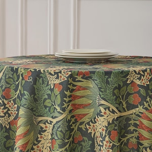 May include: A circular tablecloth featuring a dark teal backdrop adorned with a floral design in green, red, and beige hues. Two white plates are stacked on the cloth. The tablecloth is made of woven fabric.