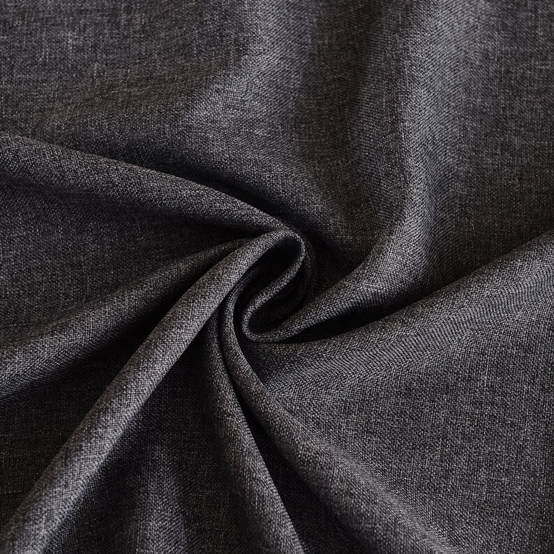 May include: A dark charcoal gray fabric with a visible woven texture and a subtle heathered appearance. The material is gathered in the center, creating deep, flowing folds and shadows that highlight the dense, interlaced weave of the textile.