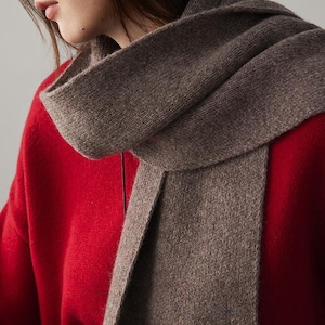 May include: A brown knitted scarf with a soft, fuzzy texture. The scarf is folded in half and draped around the neck of a person wearing a red sweater.