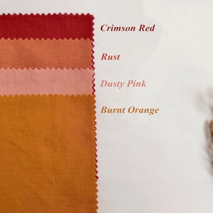 May include: Four rectangular fabric swatches with pinked edges arranged vertically. The colors are labeled as Crimson Red, Rust, Dusty Pink, and Burnt Orange. The fabric has a visible woven texture, and the text is printed next to each swatch.