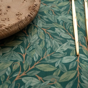 May include: Two gold forks on a green tablecloth with a leafy pattern. The tablecloth has a brown background with green leaves and branches.