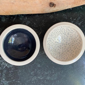 May include: Two small ceramic bowls, one with a solid dark blue glaze and the other with a white glaze and a pattern of small black lines.