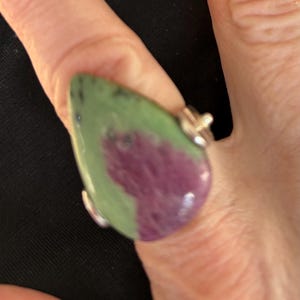May include: A teardrop-shaped ring with a green and purple gemstone set in silver.