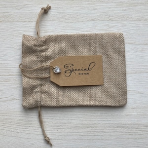 May include: A small burlap gift bag with a brown paper tag that says "To a Special Sister". A small silver heart charm is attached to the tag.