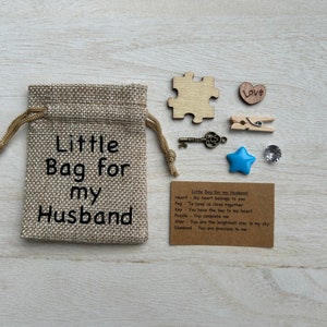 May include: A small burlap bag with the text "Little Bag for my Husband" printed on it. The bag contains a heart, a peg, a key, a puzzle piece, a star, and a diamond. A card with the text "Little Bag for my Husband" and descriptions for each item is included.