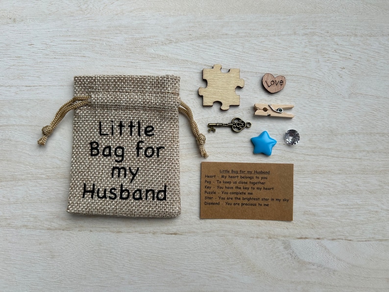 May include: A small burlap bag with the text "Little Bag for my Husband" printed on it. The bag contains a heart, a peg, a key, a puzzle piece, a star, and a diamond. A card with the text "Little Bag for my Husband" and descriptions for each item is included.