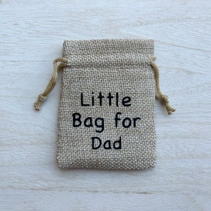 May include: A small burlap drawstring bag with the text "Little Bag for Dad" embroidered on the front.