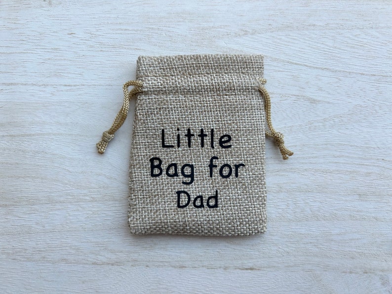 May include: A small burlap drawstring bag with the text "Little Bag for Dad" embroidered on the front.