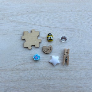 May include: A collection of small wooden and plastic decorations, including a jigsaw piece, a heart with the word "Love" on it, a bee, a flower, a star, and a clothes peg.