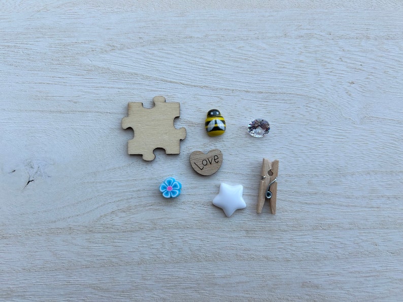 May include: A collection of small wooden and plastic decorations, including a jigsaw piece, a heart with the word "Love" on it, a bee, a flower, a star, and a clothes peg.