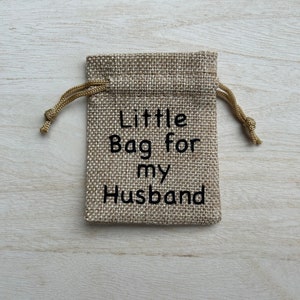 May include: A small burlap bag with a drawstring closure. The bag is decorated with the text "Little Bag for my Husband".