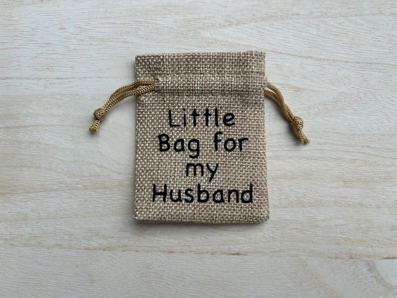 May include: A small burlap bag with a drawstring closure. The bag is decorated with the text "Little Bag for my Husband".