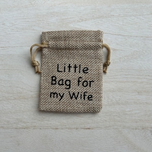 May include: A small burlap bag with a drawstring closure. The bag is decorated with the text "Little Bag for my Wife" in black embroidery.