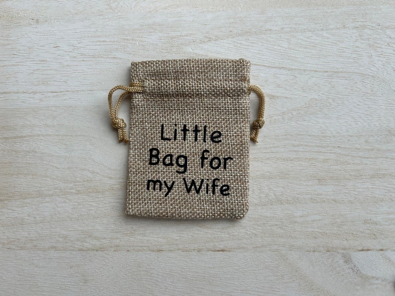 May include: A small burlap bag with a drawstring closure. The bag is decorated with the text "Little Bag for my Wife" in black embroidery.