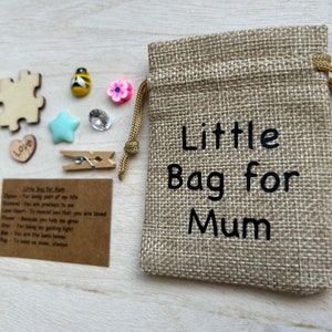 Może przedstawiać: Mały woreczek jutowy ze sznurkiem do ściągania. Woreczek jest nadrukowany tekstem "Little Bag for Mum". Woreczek jest otoczony r&oacute;żnymi małymi przedmiotami, w tym drewnianym elementem układanki, sercem, gwiazdą, pszczołą, kwiatem, spinaczem do bielizny i kartką z tekstem "Little Bag for Mum".