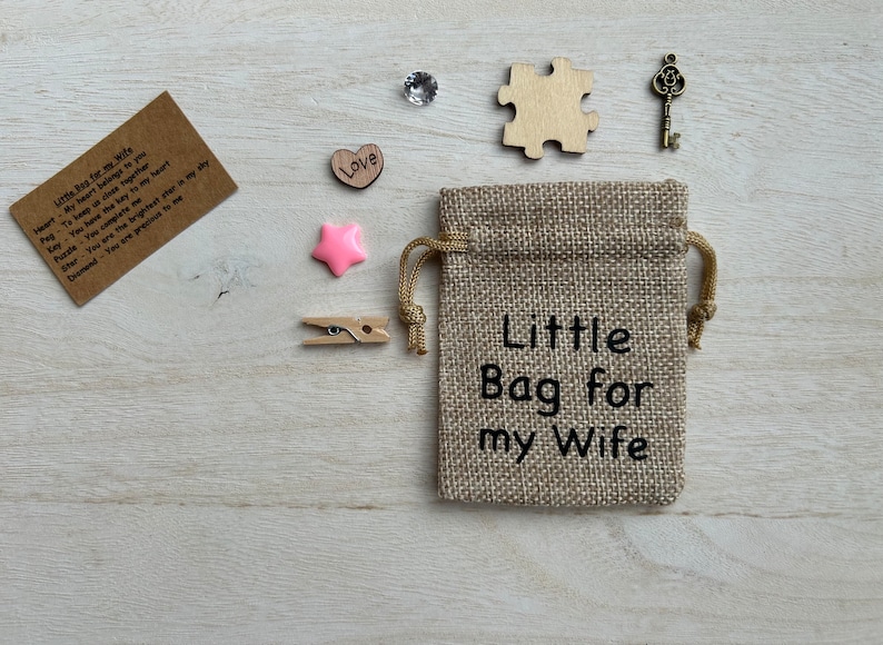 May include: A small burlap bag with the text "Little Bag for my Wife" printed on it. The bag is surrounded by various small items, including a heart, a star, a key, a puzzle piece, and a note with the text "Heart - You have the key to my heart, Pag - To keep us close together, Key - You are the key to my heart, Puzzle - You complete me, Star - You are the brightest star in my sky, Diamond - You are precious to me".