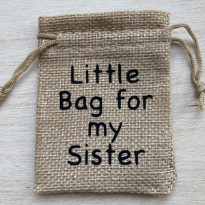 Może przedstawiać: Mały woreczek z juty ze sznurkiem do ściągania. Na woreczku znajduje się napis "Little Bag for my Sister".