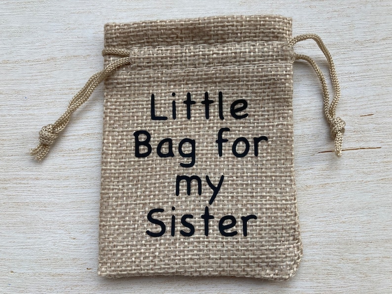 Może przedstawiać: Mały woreczek z juty ze sznurkiem do ściągania. Na woreczku znajduje się napis "Little Bag for my Sister".