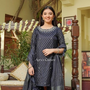 May include: A navy blue shalwar kameez with gold embroidery and a matching dupatta. The kameez has a round neckline and a dotted pattern. The shalwar is flared and has a ruffled hem. The dupatta is sheer and has a striped pattern.