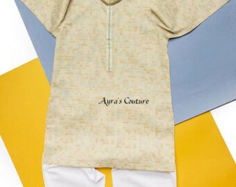 Puede incluir: Una kurta de patrón beige y blanco con ribete azul y pantalones blancos. La kurta tiene un cuello con cuentas y el texto "Ayra's Couture" está impreso en la parte delantera.