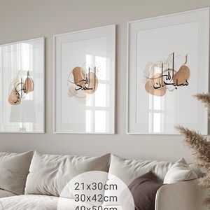 May include: Three framed prints with white mats and white frames. The prints feature abstract watercolor designs in shades of brown and beige with Arabic calligraphy in black. The prints are displayed on a wall above a white sofa.
