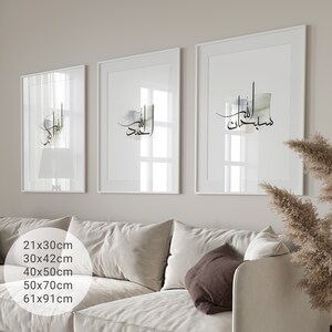 May include: Three white framed prints with Arabic calligraphy in black ink on a white background. The prints are hanging on a white wall above a white couch with brown throw pillows.