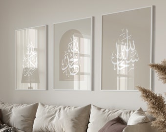 May include: Three framed prints with Arabic calligraphy in white on a beige background. The prints are hanging on a white wall above a beige couch with pillows.