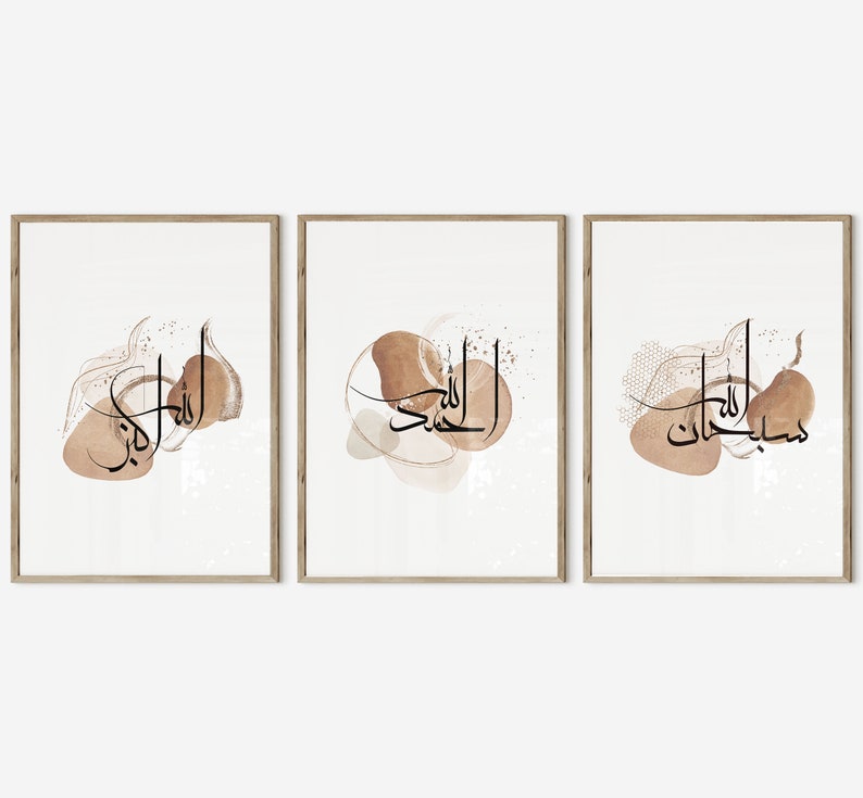 May include: Set of three framed prints with Arabic calligraphy in black on a white background. Each print features a different phrase in Arabic script, surrounded by abstract brown watercolor shapes.