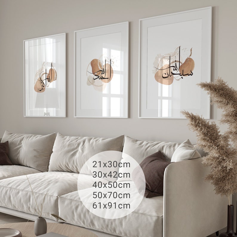 May include: Three framed prints with white mats and white frames. The prints feature abstract watercolor designs in shades of brown and beige with Arabic calligraphy in black. The prints are displayed on a wall above a white sofa.