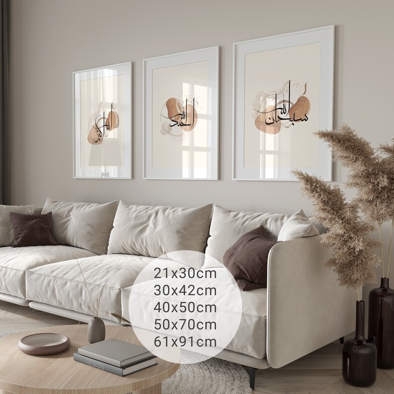 May include: Three framed prints with abstract brown watercolor designs and Arabic calligraphy. The prints are hanging on a light beige wall above a white sofa. The text on the prints reads "Subhanallah" and "Alhamdulillah".