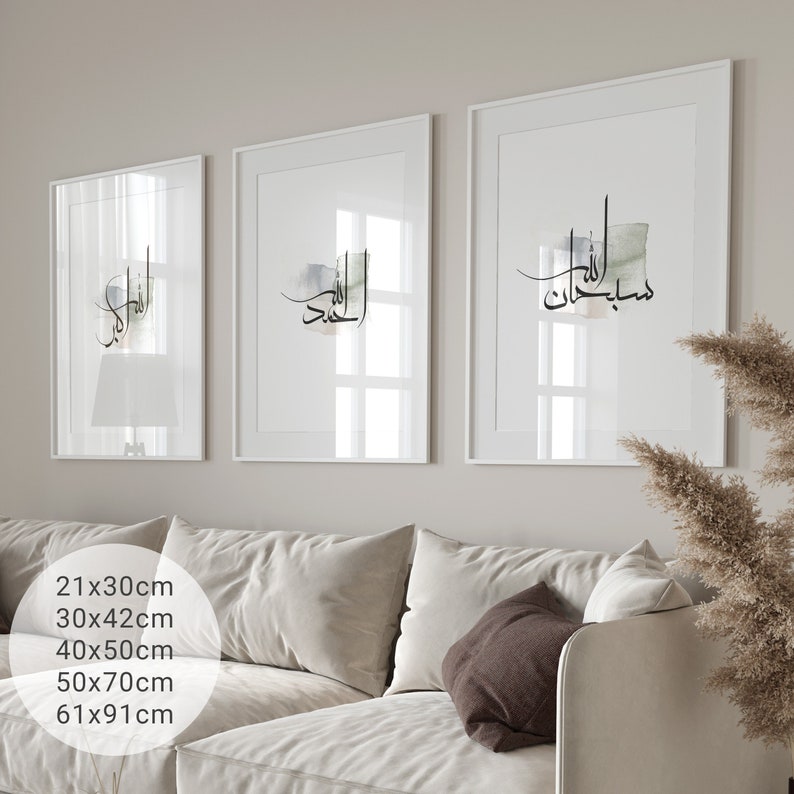 May include: Three white framed prints with Arabic calligraphy in black ink on a white background. The prints are hanging on a white wall above a white couch with brown throw pillows.