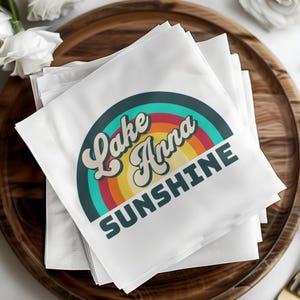 White cocktail napkins with "Lake Anna Sunshine" text and rainbow logo.