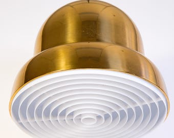 May include: A modern, gold-colored pendant light fixture with a white, circular, slatted diffuser. The light has a rounded, two-tiered design and hangs from a black cord against a white background. The fixture is a decorative lighting element.