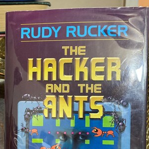 May include: A book titled "The Hacker and the Ants" by Rudy Rucker. The cover features a retro computer screen with a game-like design, orange ant-like creatures, and the number 2500. The background is a dark purple.
