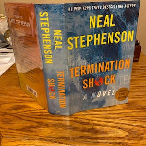 May include: A hardcover book titled "Termination Shock" by Neal Stephenson. The cover features blue and orange text against a blue and white background. The book is a signed first edition.