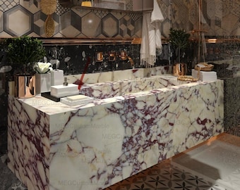 Può includere: Un mobile da bagno con piano in marmo e doppio lavabo. Il mobile è decorato con un motivo a piastrelle geometriche e due luci a parete con paralumi gialli. Il mobile è realizzato in marmo chiaro con venature rosso scuro.