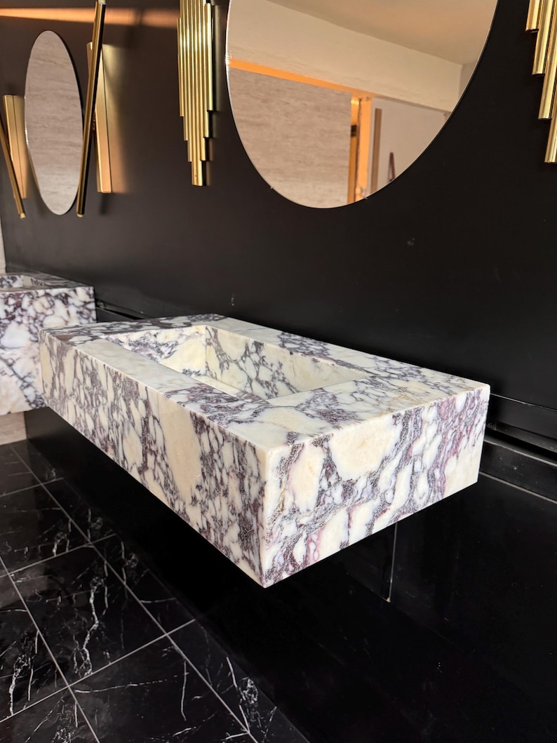 A calacatta viola marble sink with brown and purple veins. The sink is rectangular and has a square basin. The sink is sitting on a white surface.