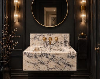 May include: A luxurious bathroom interior featuring a marble sink with gold fixtures, a round gold-framed mirror, and sconces. The walls are dark, and the floor has a marble pattern. A black vase with branches is on the left.
